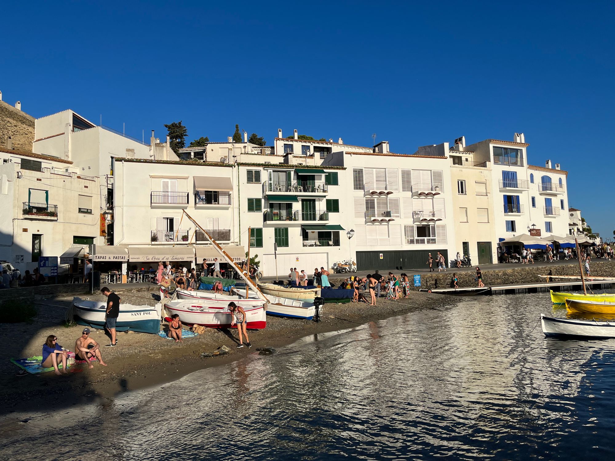 white buildings on the bay front, colorful boats and people are on the shore