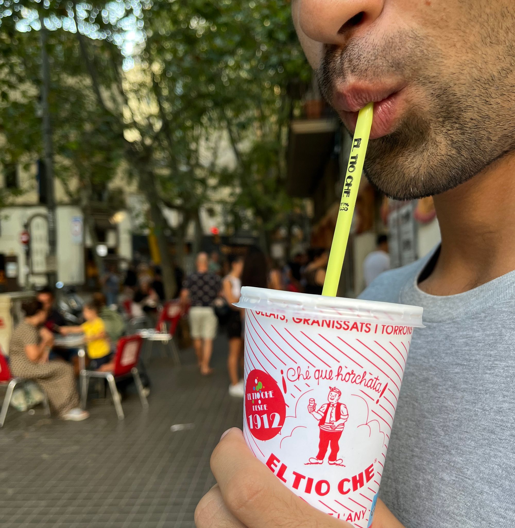 a close up of a man sipping horchata from a paper cup with a straw