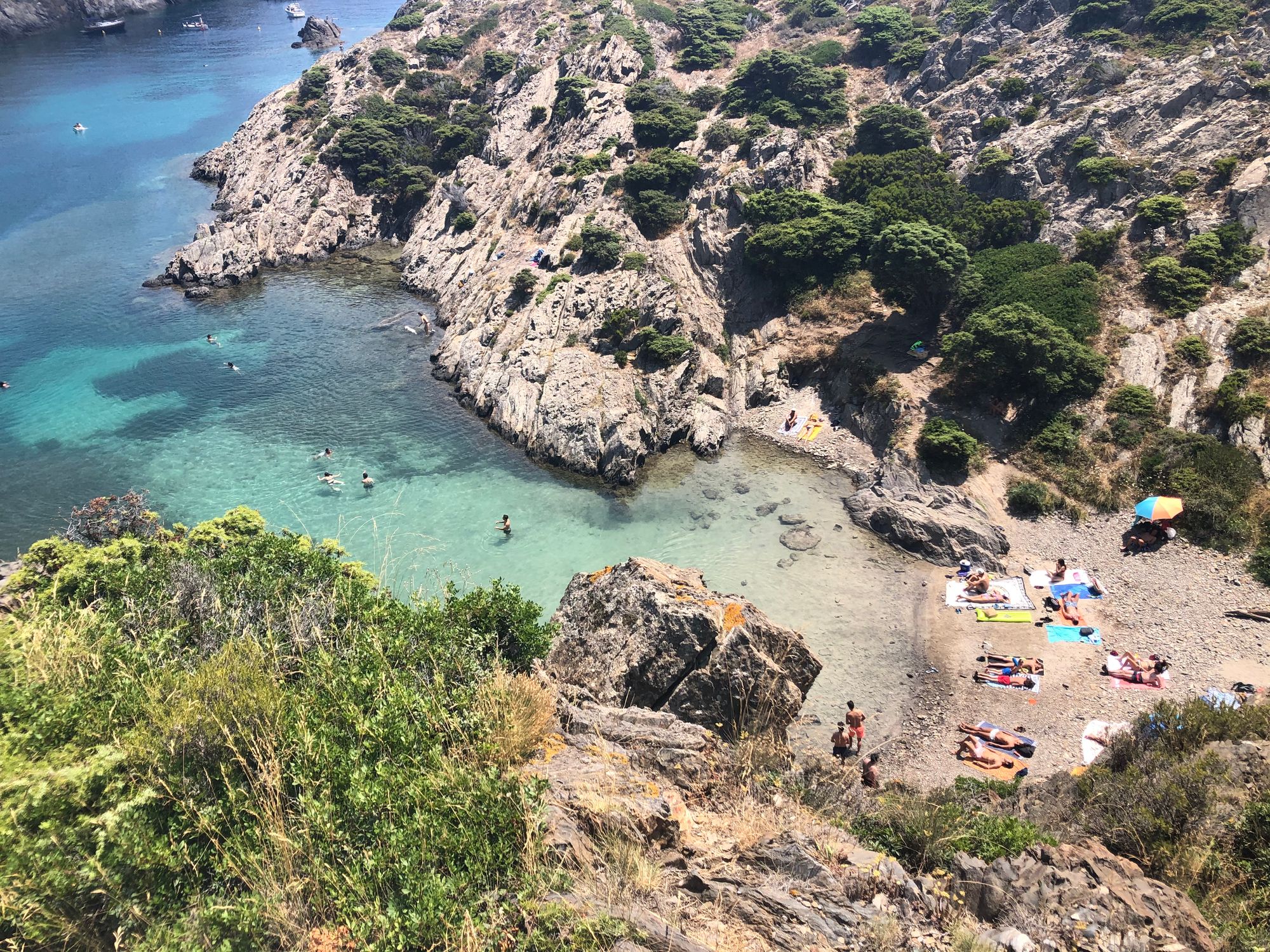 aerial view of a cove with some people sunbathing. turqouise waters between rocky cliffs and shrubs 