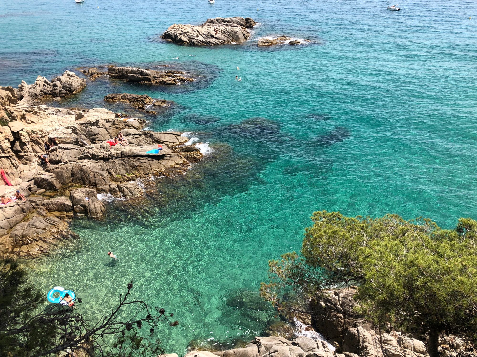 rocky outcrops fading into clear turquoise waters with sun bathers and swimmers